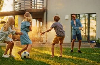 Vater spritzt Kinder mit einem Wasserschlauch im Garten nass